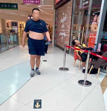 2019년 7월 23일 중국 베이징의 쇼핑몰에서 한 남성이 남색 티셔츠를 걷어올리고 배를 드러낸 채 걷고 있다. 오른쪽으로는 배달 업체 유니폼을 입은 직원이 의자에 앉아 배를 보인 채 자고 있다. /베이징=김남희 특파원