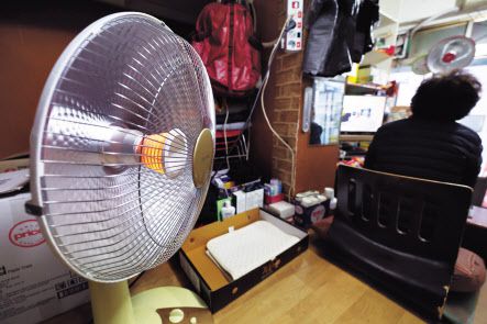 정부가 ‘난방비 폭탄’으로 어려움을 겪는 모든 기초생활수급자와 차상위 계층에 올겨울 난방비를 지원하기로 한 1일 서울 중구의 한 가게에서 상인이 전기난로로 추위를 피하고 있다. [연합]