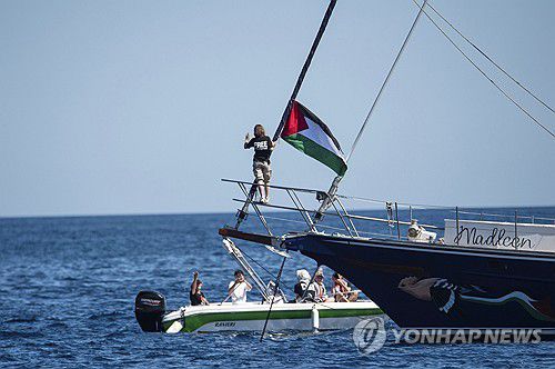 (카타니아 <이탈리아 시칠리아섬> AP=연합뉴스) 2025년 6월 1일 기후변화 활동가 그레타 툰베리(사진 가운데)가 '자유선단연합' 소속 매들린호에 타서 배에 걸린 팔레스타인 국기 옆에 서 있다. (AP Photo/Salvatore Cavalli) 2025.6.8.