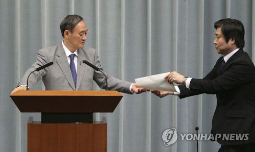 스가 요시히데(菅義偉) 관방장관이 기자회견 중 비서관으로부터 답변 요지가 적힌 종이를 전달받고 있다. [교도=연합뉴스 자료사진]