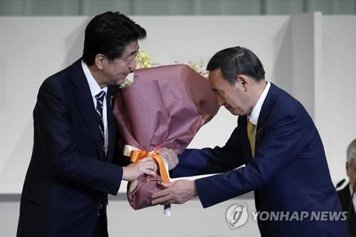 아베에게 꽃다발 주는 스가[AP=연합뉴스 자료사진]