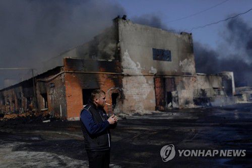 러시아군 포격으로 불타는 우크라 하르키우 공장 건물(하르키우 로이터=연합뉴스) 지난달 30일(현지시간) 러시아군의 포격으로 불타고 있는 우크라이나 하르키우의 한 공장 주변에서 한 남성이 담배를 피고 있다. 2022.5.1 jsmoon@yna.co.kr