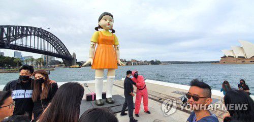 호주 시드니에 등장한 오징어게임 '영희' 인형(시드니=연합뉴스) 정동철 통신원 = 호주 넷플릭스가 2021년 10월 29일부터 11월 1일까지 4일간 시드니의 명소 오페라 하우스와 하버 브리지 사이에 '무궁화꽃이 피었습니다' 게임의 술래 '영희' 인형과 분홍색 제복의 진행 요원 등 '오징어 게임' 체험장을 설치해 현지인들의 뜨거운 호응을 받았다.      나흘간 1만 명 가량의 인파가 체험장을 찾아 호주에서의 '오징어 게임' 인기를 실감할 수 있었다.      사진은 1일 호주 시드니하버에 설치된 영희 인형을 찾은 시민들의 모습. 2021.11.1 dcj@yna.co.kr