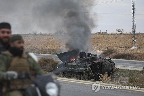 시리아 남부 하마에서 불타는 정부군 장갑차 옆으로 반군이 지나가고 있다. [AP=연합뉴스]
