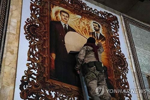 철거되는 알아사드 형제 포스터 (AFP=연합뉴스) 시리아 반군이 알레포 공항에서 대통령 바샤르 알아사드(왼쪽)와 그의 동생 마헤르가 그려진 포스터를 떼어내고 있다. [재판매 및 DB금지]