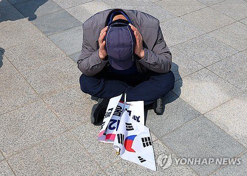 윤석열 전 대통령 파면, 고개 숙인 지지자(서울=연합뉴스) 김도훈 기자 = 헌재의 윤석열 전 대통령 탄핵 인용이 발표된 4일 서울 용산 대통령실 인근에서 낙담한 지지자가 땅바닥에 앉아 허탈해 하고 있다. 2025.4.4 superdoo82@yna.co.kr