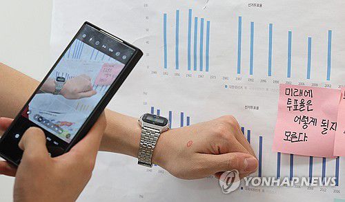 '투표율 높였어요'(대구=연합뉴스) 윤관식 기자 = 제21대 대통령 선거일인 3일 대구 중구 동덕초등학교 1층 드라마실에 마련된 삼덕동 제2투표소에서 투표를 마친 유권자들이 투표소 밖 게시판에 붙어있는 초등학생들의 투표율 분석 게시물 앞에서 '투표 인증샷'을 남기고 있다. 2025.6.3 psik@yna.co.kr