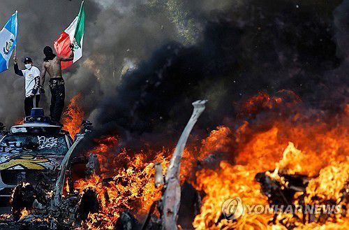 LA에서 차량이 불타고 있는 가운데 깃발을 든 불법이민자 단속 반대 시위대 [AFP=연합뉴스 자료사진. 재판매 및 DB금지]