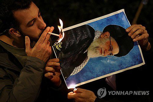 영국 런던에서 열린 시위 중 한 남성이 이란 최고지도자 아야톨라 알리 하메네이의 사진에 붙은 불을 이용해 담뱃불을 붙이고 있다.[로이터 연합뉴스 자료사진. 재배포 및 DB 금지]