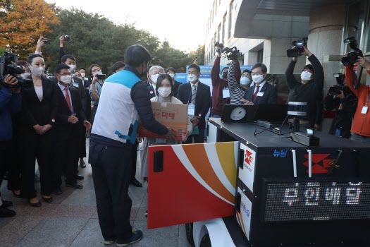 28일 오후 세종특별자치시 고려대학교 세종캠퍼스에서 열린 `우정사업 자율주행 시범운영 행사`에서 집배원이 추종로봇에서 무거운 소포를 꺼내 고객에게 전달하고 있다.(사진=과학기술정보통신부 제공)