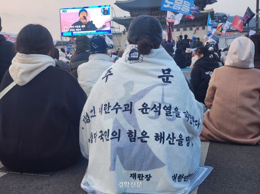 윤석열 대통령에 대한 탄핵을 촉구하는 집회 참가자가 8일 오후 서울 종로구 광화문 인근에서 ‘윤 대통령을 파면한다’는 내용 등이 적힌 담요를 덮고 앉아 있다. 우혜림 기자