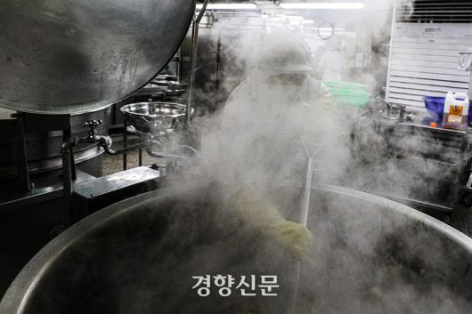 한 급식 조리사가 보다 큰 솥 앞에 서서 뜨거운 김을 맞으며 조리용 삽으로 돼지갈비찜을 뒤집고 있다. 성동훈 기자