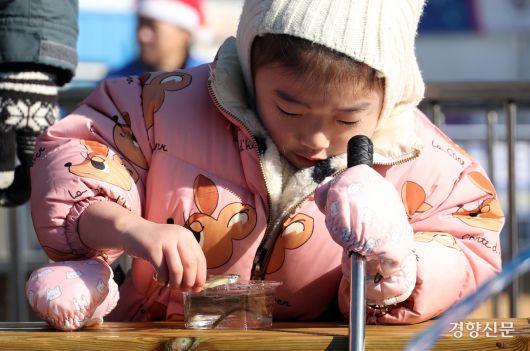 한 어린이가 빙어를 잡아 통에 담고 있다.