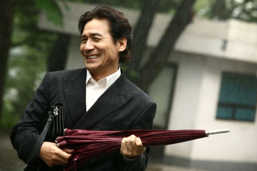 영화 <라디오스타>에서 매니저 박민수 역할을 맡은 배우 안성기가 우산을 들고 환하게 웃고 있다. 시네마서비스 제공