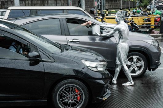 지난달 1일 인토네시아 자카르타의 한 도로에서 온몸을 은색 페인트로 칠한 아리 무난다르가 비를 맞으며 운전자에게 구걸하고 있다. AFP 연합뉴스