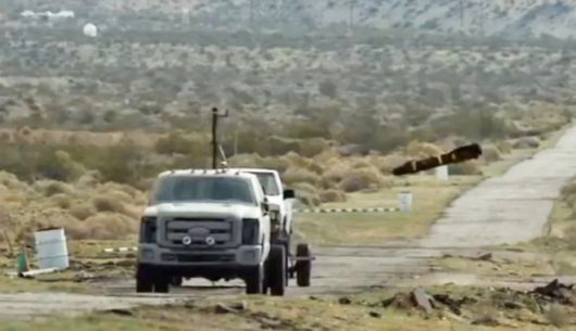 미 공군 훈련장에서 헬파이어 미사일이 표적 차량을 향해 낙하하는 장면. 실험 장비가 장착된 트럭이 표적 차량을 견인하고 있으며, 공중에서 날아든 AGM‑114 헬파이어(Hellfire) 미사일이 곧 충돌하는 순간이 포착됐다. 해당 사진은 미국 국방부 훈련 영상에서 캡처된 것으로, 실제 공대지 미사일 정밀 타격 훈련 장면이다. 출처=미국 국방부 퍼블릭 도메인