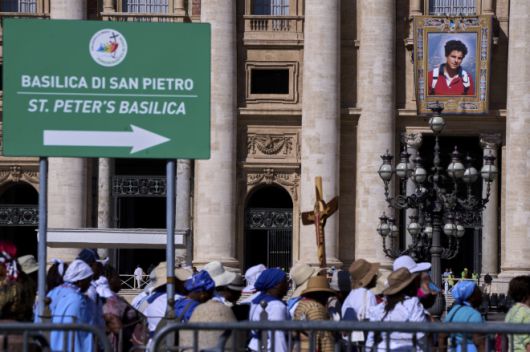 7일(현지시간) 시성식을 앞두고 바티칸 성 베드로 대성당 외벽에 걸린 카를로 아쿠티스의 대형 태피스트리. 순례객들이 희년 행사에 맞춰 성문을 통과하고 있다. AP 연합뉴스