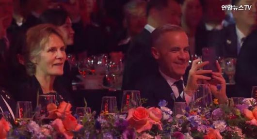 마크 카니(왼쪽) 캐나다 총리가 31일 경북 경주 라한셀렉트호텔 대연회장에서 열린 ‘2025 APEC 정상회의’ 환영 만찬 공연 무대에 오른 가수 지드래곤을 휴대폰 카메라로 촬영하고 있다. 2025.10.31 연합뉴스TV 화면