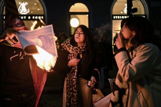 밀라노 미국 영사관 밖에서 반이란 정권 시위대가 이란 최고 지도자 알리 하메네이의 모습을 담은 불붙은 종이로 담배에 불을 붙이고 있다. 2026.1.14 AFP 연합뉴스