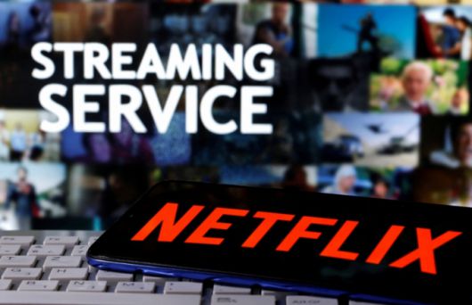 A smartphone with the Netflix logo is seen on a keyboard in front of displayed "Streaming service" words in this illustration taken March 24, 2020. REUTERS/Dado Ruvic/File Photo