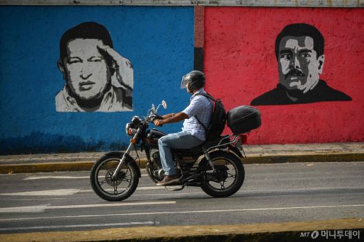지난해 9월 26일 한 바이커가 우고 차베스 전 대통령과 니콜라스 마두로 현 대통령의 벽화가 그려져 있는 카라카스 거리를 달리고 있다. 대선 결과를 둘러싼 정정 불안이 지속되는 가운데 공식 달러 환율과 암시장 시세간 차가 점차 커지며 이전의 고(高)인플레이션 사태가 재연될 우려가 커지고 있다. /AFPBBNews=뉴스1