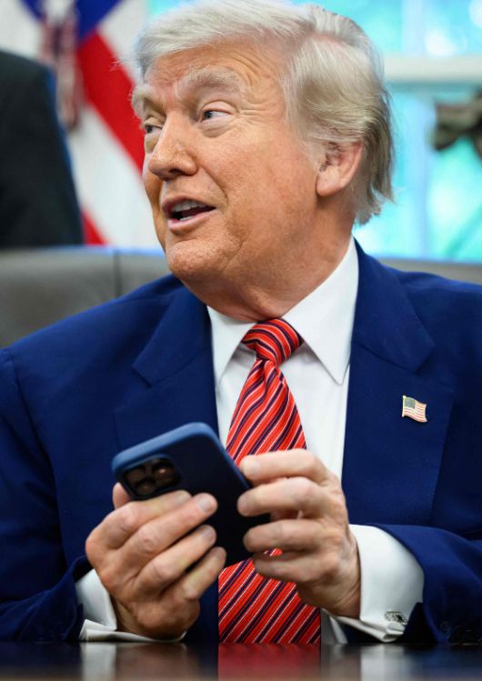 도널드 트럼프 미국 대통령이 지난 23일(현지시간) 워싱턴 백악관에서 행정 명령에 서명을 하면서 취재진과 질의응답을 하던 도중 아이폰 벨 소리가 울리자 '무음 모드'로 바꾸고 있다. /AFPBBNews=뉴스1