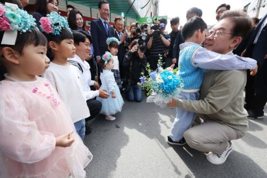 이재명 더불어민주당 대선후보(오른쪽)가 6일 충북 증평군 증평장뜰시장에서 진행된 '골목골목 경청투어' 유세 도중 어린이에게 꽃다발을 받은 뒤 안고 있다. 연합뉴스