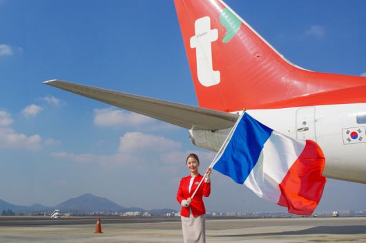 티웨이항공 승무원이 티웨이항공 항공기 앞에서 '인천~파리' 노선 취항 1년을 기념해 프랑스 국기를 들고 포즈를 취하고 있다. 티웨이항공 제공