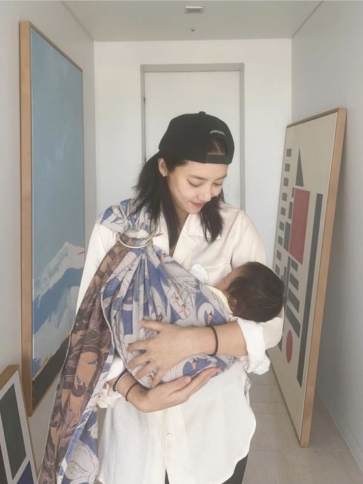 흰 셔츠에 블랙 모자를 푹 눌러쓴 손담비는 아기 해이를 품에 안고 있는 모습.사진=손담비 SNS