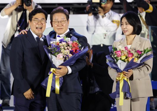 제21대 대통령에 당선된 이재명 대통령과 부인 김혜경 여사가 지난 4일 서울 여의도 국회 인근에서 당 주최로 열린 국민개표방송 행사에 참석해 박찬대 민주당 당대표 직무대행 겸 원내대표에게 꽃다발을 받고 있다. [사진 출처 = 연합뉴스]