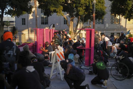 시위대가 전날 밤의 이민 단속 항의 시위에 이어, 2025년 6월 8일 일요일 로스앤젤레스 다운타운의 메트로폴리탄 구치소 근처에서 벤치 뒤에 몸을 숨기고 있다. [사진 = AP 연합뉴스]