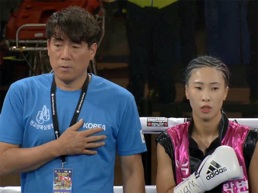 대전변교선복싱클럽 변교선 관장과 박혜수가 2025년 6월 이탈리아 노바라 ‘팔라이고르 고르곤촐라’ 세계복싱협회 여자 플라이급 골드타이틀매치 시작 전 태극기에 경례하며 애국가를 부르고 있다. 사진=이탈리아복싱연맹(Federazione Pugilistica Italiana) 영상 화면