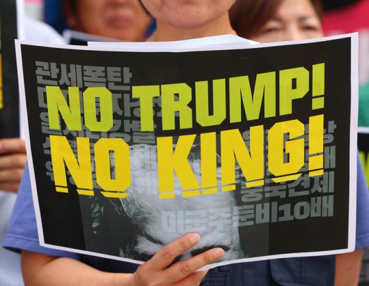 한미 관세협상이 타결된 31일 서울 광화문 미국대사관 인근에서 트럼프위협저지공동행동 및 농민의길 주최로 열린 입장발표 기자회견에서 한 참가자가 피켓을 들고 있다. [사진  = 연합뉴스]