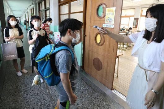 여름방학을 마치고 개학한 18일 오전 대구의 한 초등학교 교실 앞에서 담임 교사가 학생들의 체온을 측정하고 있다. 뉴스1