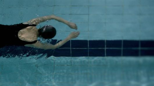 성폭행 사건 후 수영하는 효정의 뒷모습. 임선애 감독은 "효정에게 수영은 무릎 관절 때문에 그나마 할 수 있는 운동이고 마지막 돌파구"라면서 "사건 경험 직후엔 효정이 팔다리를 움직일 수 없을 만큼 무력감이 들지 않을까, 생각해 물에 몸을 맡긴 채 죽은 듯이 떠가는 이미지를 만들고 싶었다"고 했다. 수영은 그가 "실제 주변 장년 여성들이 무리 없는 운동으로 즐기는 걸 보고 택한 설정"으로, "가라앉지 않으려면 팔다리를 열심히 움직여야만 하고 몸을 움직여야 어떤 목표에 도달하게 된다"는 수영의 속성은 성폭행 사건 후 효정의 고군분투와 연결되기도 한다. [사진 엣나인필름]