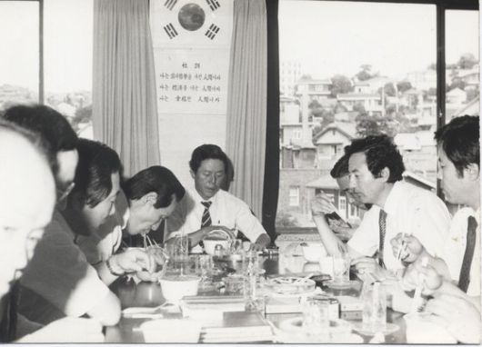 농심 임직원들과 당시 신제품이던 컵라면을 맛보고 있는 故 신춘호 회장(가운데). '나는 삶의 철학을 가진 인간이다', '나는 경제를 아는 인간이다', '나는 행복한 인간이다'라는 농심의 사훈이 벽에 걸려있다. 사진 농심