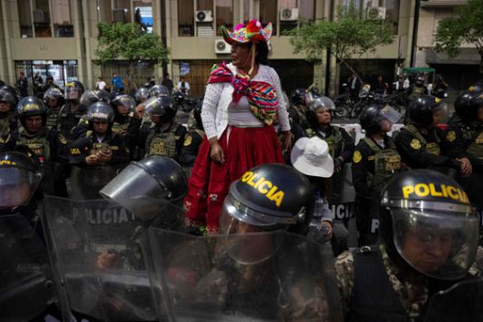 지난 14일(현지시간) 페루 리마에서 정부 반대 시위가 벌어지는 동안 원주민 여성이 진압 경찰들 사이에 서 있다. AFP=연합뉴스