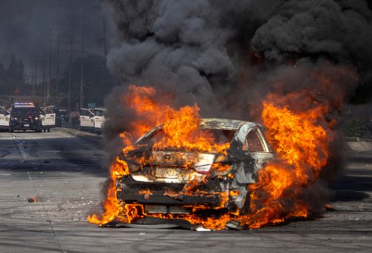 미국 캘리포니아주 로스앤젤레스 카운티 파라마운트에서 7일(현지시간) 이민 및 세관 집행국(ICE)에 의한 여러 건의 구금 이후 경찰과 시위대 간의 대치 상황에서 시위대가 파괴된 차량 위에서 멕시코 깃발 등을 흔들고 있다. 로이터=연합뉴스