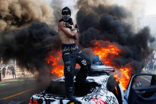 지난 8일 LA 도심 시위 현장에서 불에 타는 차량 위에 한 시위자가 올라가 있다. AFP=연합뉴스