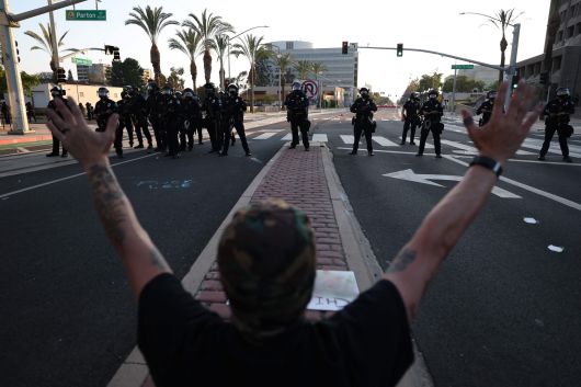 지난 6월 9일(현지시간) 미국 캘리포니아주 산타아나에서 이민·관세 집행국(ICE)의 급습 소식이 전해진 후, 한 시민이 미국 시민권·이민 서비스국(USCIS) 산타아나 지역 사무소 밖에서 경찰 대열을 향해 손을 들어 올리고 있다. AFP=연합뉴스