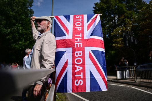 지난달 23일(현지시간) 영국 런던 남쪽 호를리에 있는 난민 수용 시설로 추정되는 쉐라톤 포 포인츠 호텔 밖에서 열린 반이민 시위에서 한 시민이 '배를 멈춰라(Stop The Boats)'라고 쓰인 영국 국기를 들고 있다. AFP=연합뉴스