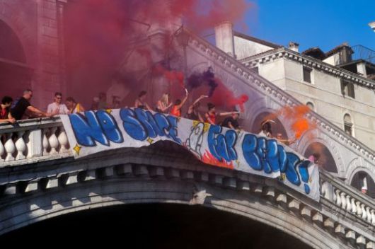 28일(현지시간) 이탈리아 베네치아 리알토 다리에서 시위대가 '베이조스를  위한 공간은 없다'라고 쓰인 현수막 옆에 서서 연기나는 불꽃을 들고 있다. 로이터 연합뉴스
