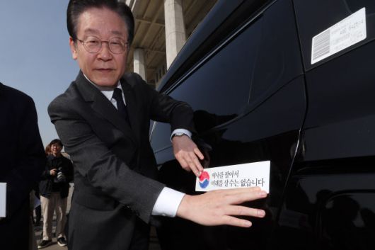 이재명 더불어민주당 대표가 22일 서울 여의도 국회에서 대일굴종외교 규탄 태극기달기 운동 행사의 일환으로 차량에 태극마크와 ‘역사를 팔아서 미래를 살 수는 없습니다’라고 적힌 스티커를 부착하고 있다.(사진=뉴스1)