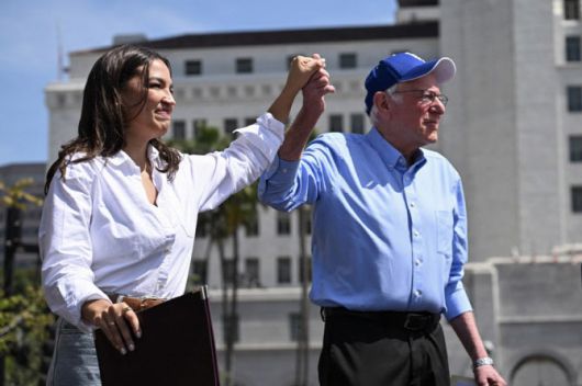 버니 샌더스 상원의원(오른쪽)과 뉴욕주 민주당 소속 알렉산드리아 오카시오 코르테스 하원의원이 지난 4월12일 로스앤젤레스의 글로리아 몰리나 그랜드 파크에서 열린 ‘과두정에 맞서 싸우며: 우리가 나아갈 길’ 집회에 함께 도착하며 손을 맞잡고 있다. (사진=AFP)