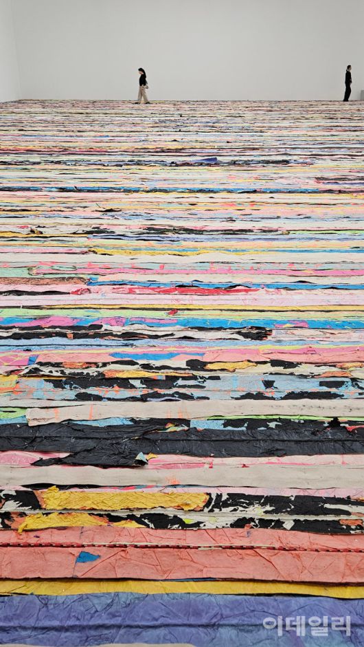 [‘2025년 미술계’ 한 장면③] 이 시대를 대표하는 현대미술 작가로 꼽히는 마크 브래드포드의 ‘떠오르다’(Float 2019) 부분. 서울 용산구 아모레퍼스픽미술관 전시장의 한 바닥 전체를 덮은 회화설치작품이다. 거리에서 주은 전단지·포스터·신문지 등을 긴 띠로 잘라내고 노끈으로 이어냈다. ‘본다’를 넘어 ‘밟고 걸어야’ 감상했다고 할 작품은 ‘계속 걷다’란 뜻의 ‘킵 워킹’(Keep Walking)이란 전시 타이틀과 이어진다(사진=오현주 문화전문기자).
