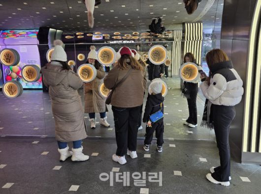 외국인 관광객들이 롯데면세점 스타에비뉴 ‘하이파이브 존’에서 한류 스타 핸드프린팅을 감상하며 사진을 촬영하고 있다. 거울 벽과 조명 연출이 셀카 명소로도 활용되고 있다. (사진=한전진 기자)
