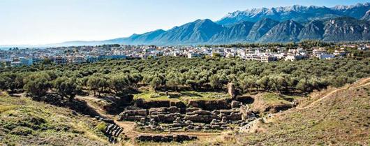 옛 스파르타의 고고학 유적지에 서면 험준한 타이게투스 산맥을 배경으로 현대 스파르타 시의 도심이 보인다. 사진 속의 토대뿐인 극장 터가 그나마 고고학 유적지에서 가장 잘 보존된 곳이다.