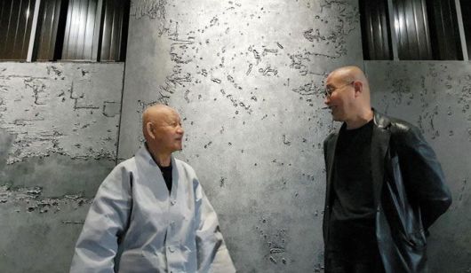 통도사 방장 성파 스님(왼쪽)과 김아타 작가. 김 작가는 성파 스님으로부터 받은‘아타’라는 법명을 작가명으로 쓰고 있으며, 22년 전 스님과 만남에서 삭발한 후 지금까지 머리를 깎은 채 지낸다. 두 사람 뒤로 보이는 것은 포사격을 받아 찢어진 캔버스를 수거해 만든 김씨의 작품. /김한수 기자