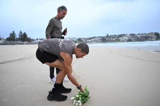 영국의 육상선수 윌리엄 굿지가 19일 호주 시드니 본다이 비치 결승선을 통과한 후 아버지와 함께 고인이 된 어머니를 추모하며 본다이 비치 해안가에 백합 꽃다발을 놓는 모습. /EPA 연합뉴스