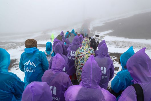 지난 11일 백두산 정상(북파)에서 관광객들이 우비를 입고 지나는 모습. /박성원 기자